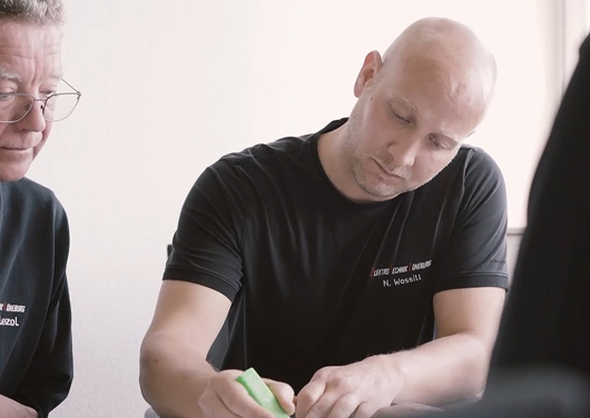 Mann mit Glatze markiert mit grünem Textmarker auf Papier, andere Person schaut zu.
