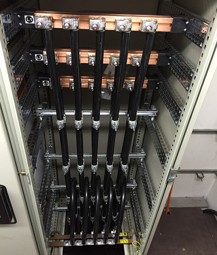 Elektrischer Schaltschrank mit schwarzen Kabeln und Kupferverbindungen.