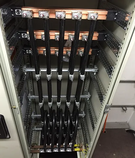 Elektrischer Schaltschrank mit schwarzen Kabeln und Kupferverbindungen.