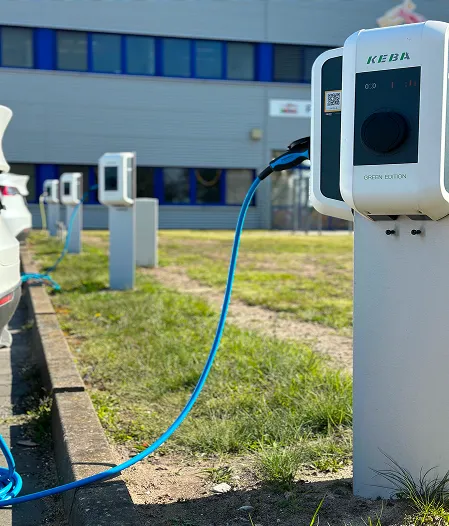 Elektroauto an Ladestation mit blauem Ladekabel an Bürogebäude im Hintergrund