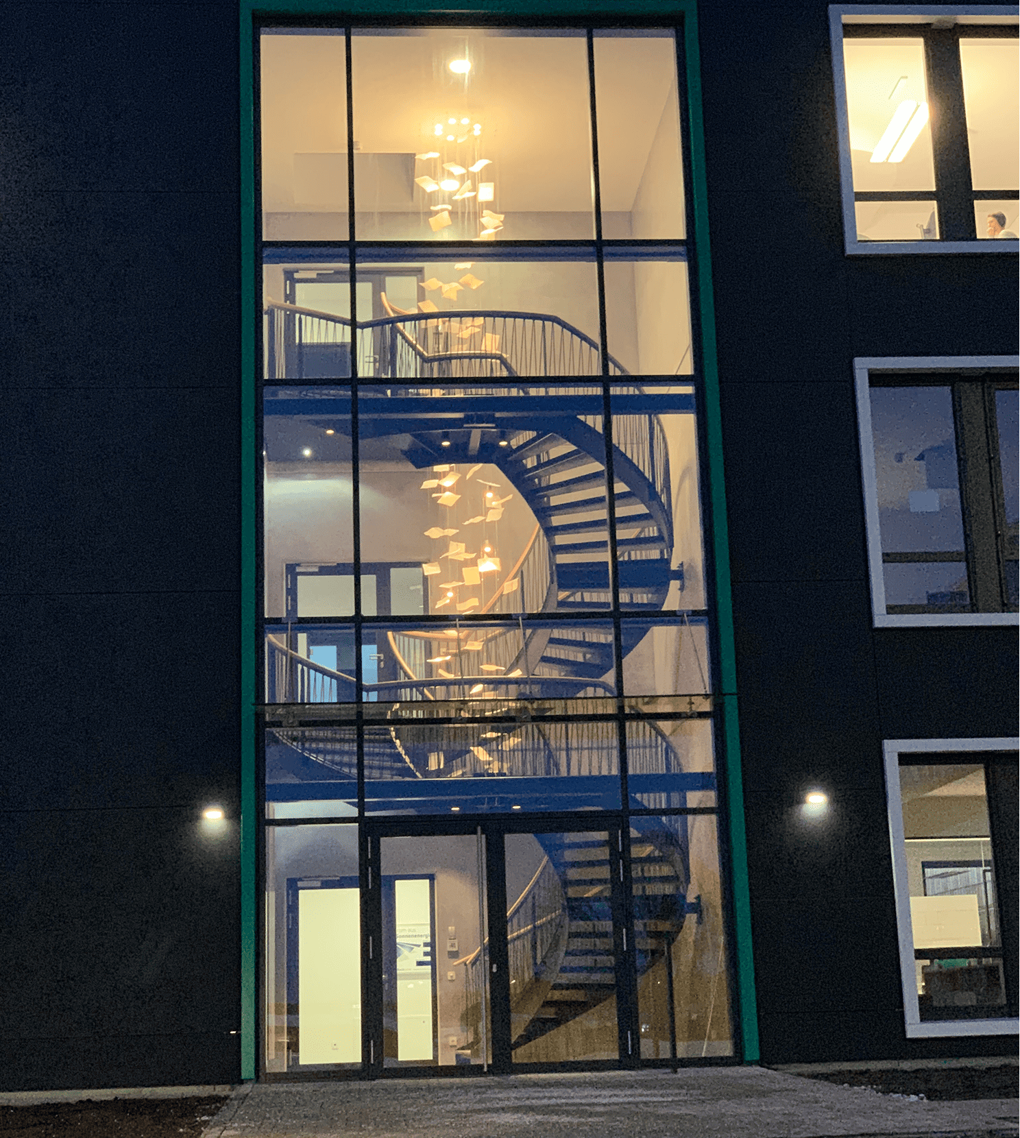 Beleuchtetes Treppenhaus mit spiralförmiger Treppe und hängender Dekoration aus Papierbögen bei Nacht.