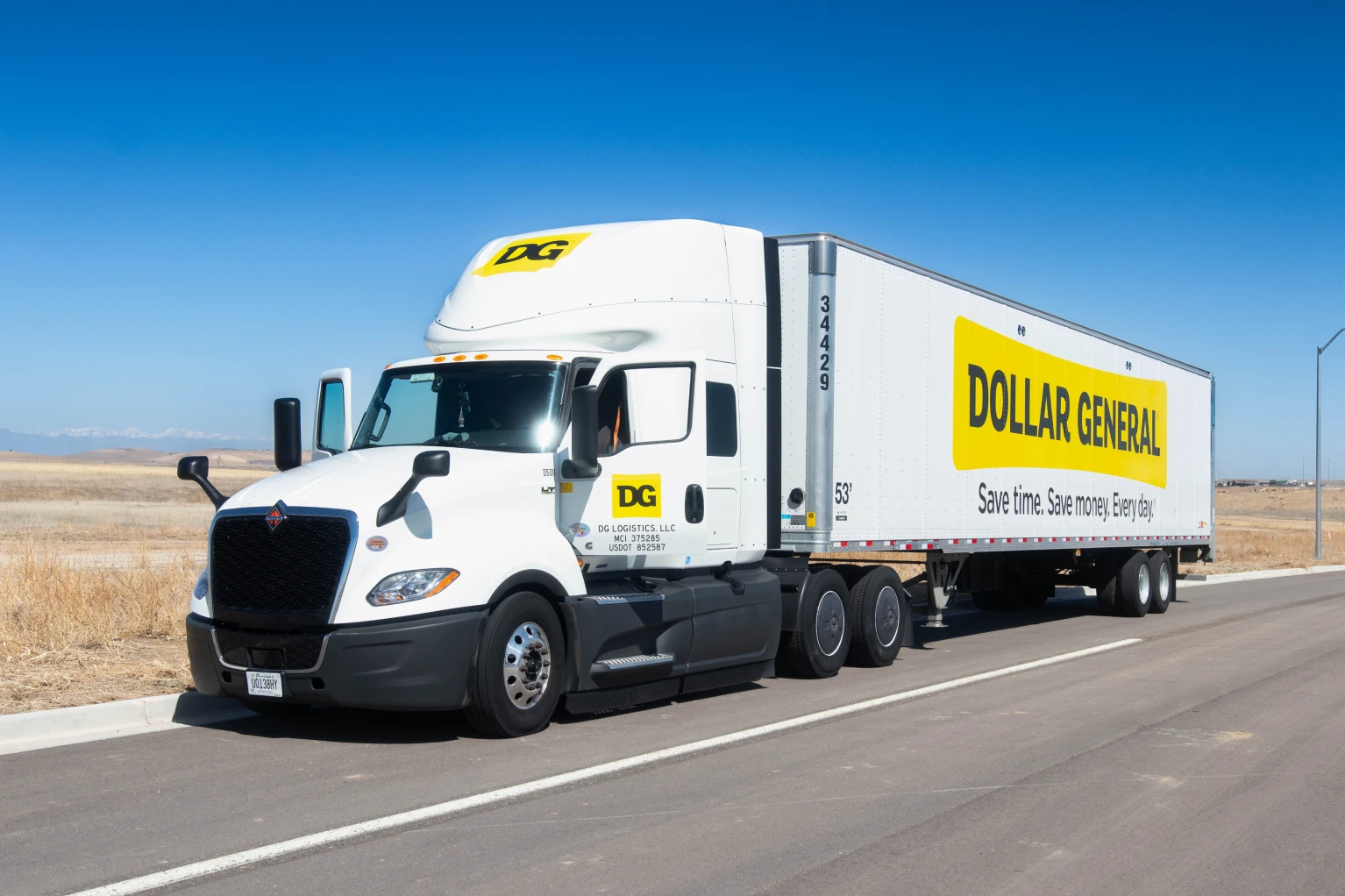 White DG logistics semi truck with Dollar General trailer parked on road with clear blue sky.