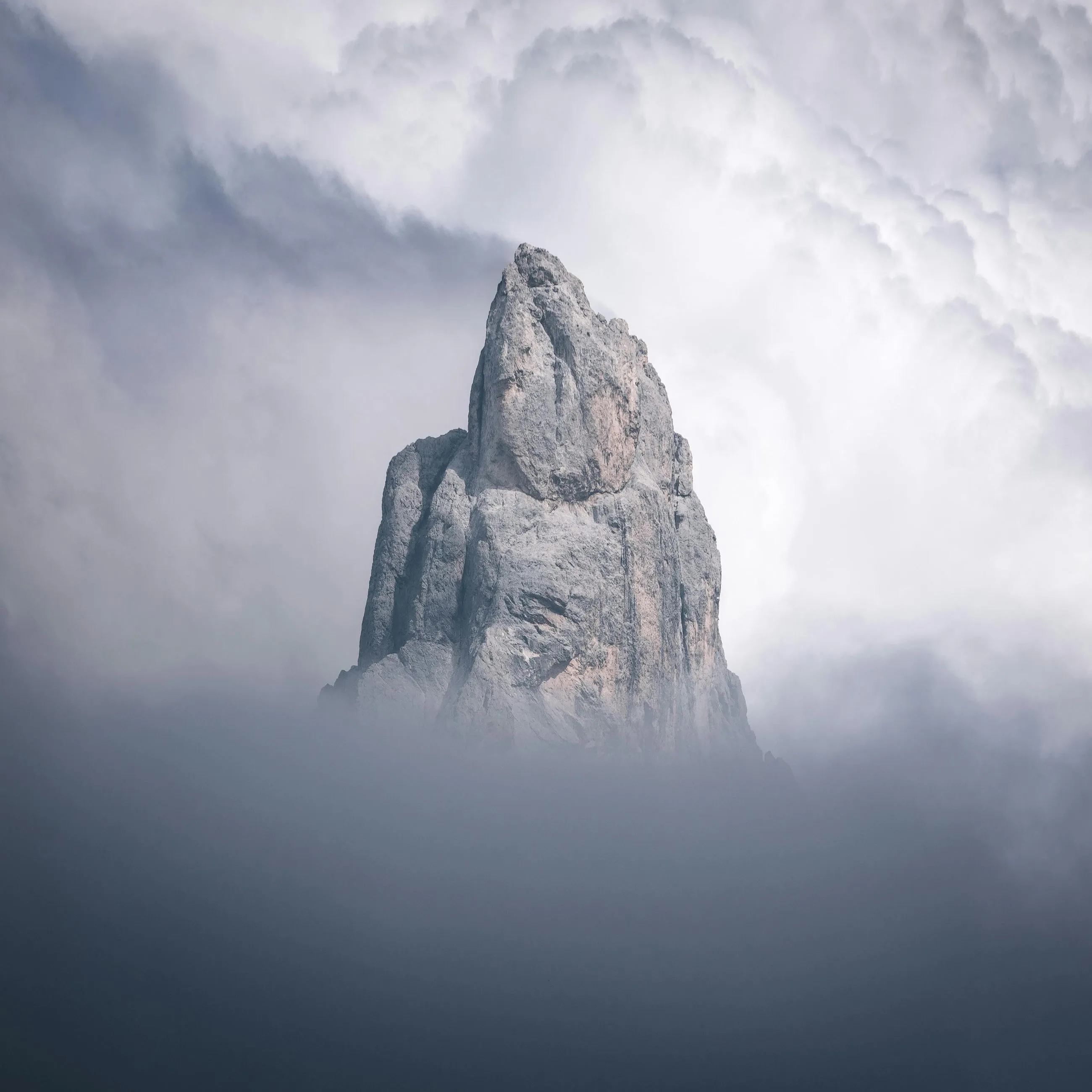 Jagged mountain peak emerging through thick fog under a cloudy sky.