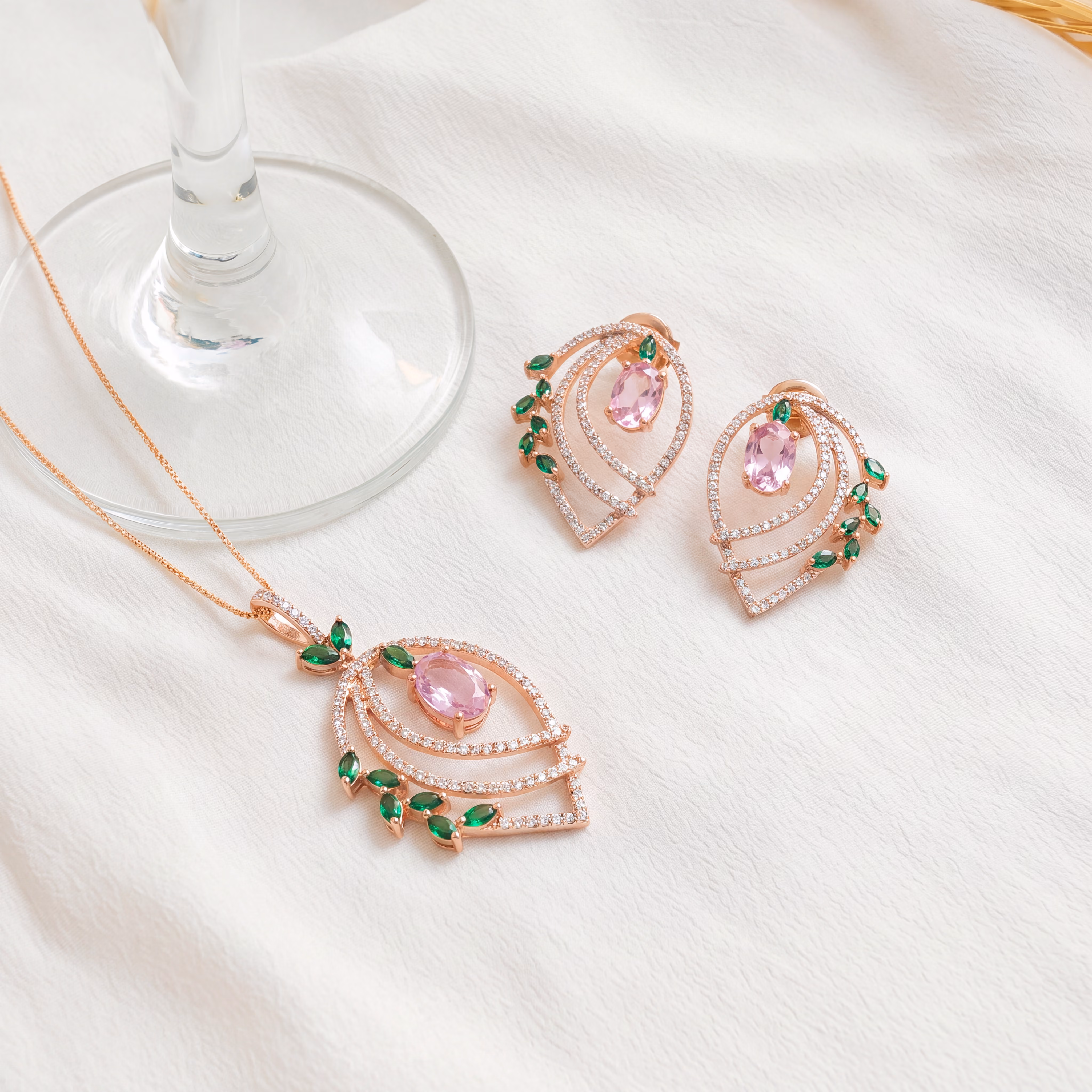 Rose gold necklace and earrings with pink oval gems, small green leaf-shaped gems, and diamonds.