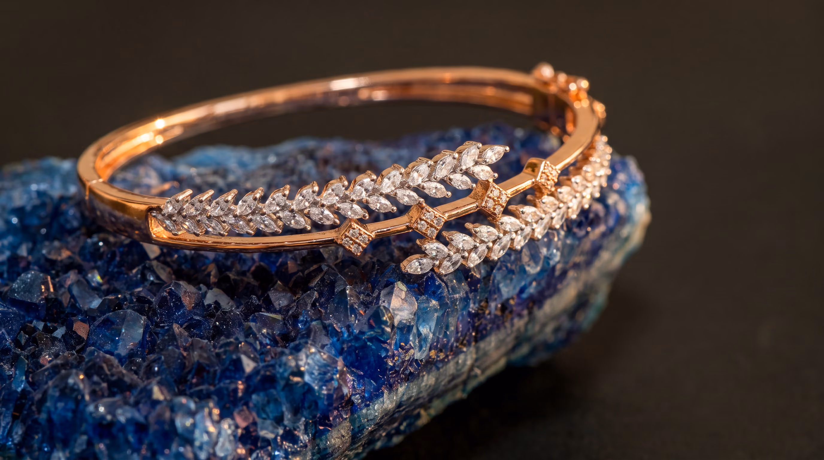 Rose gold bracelet with leaf-shaped diamonds resting on a blue crystal rock.