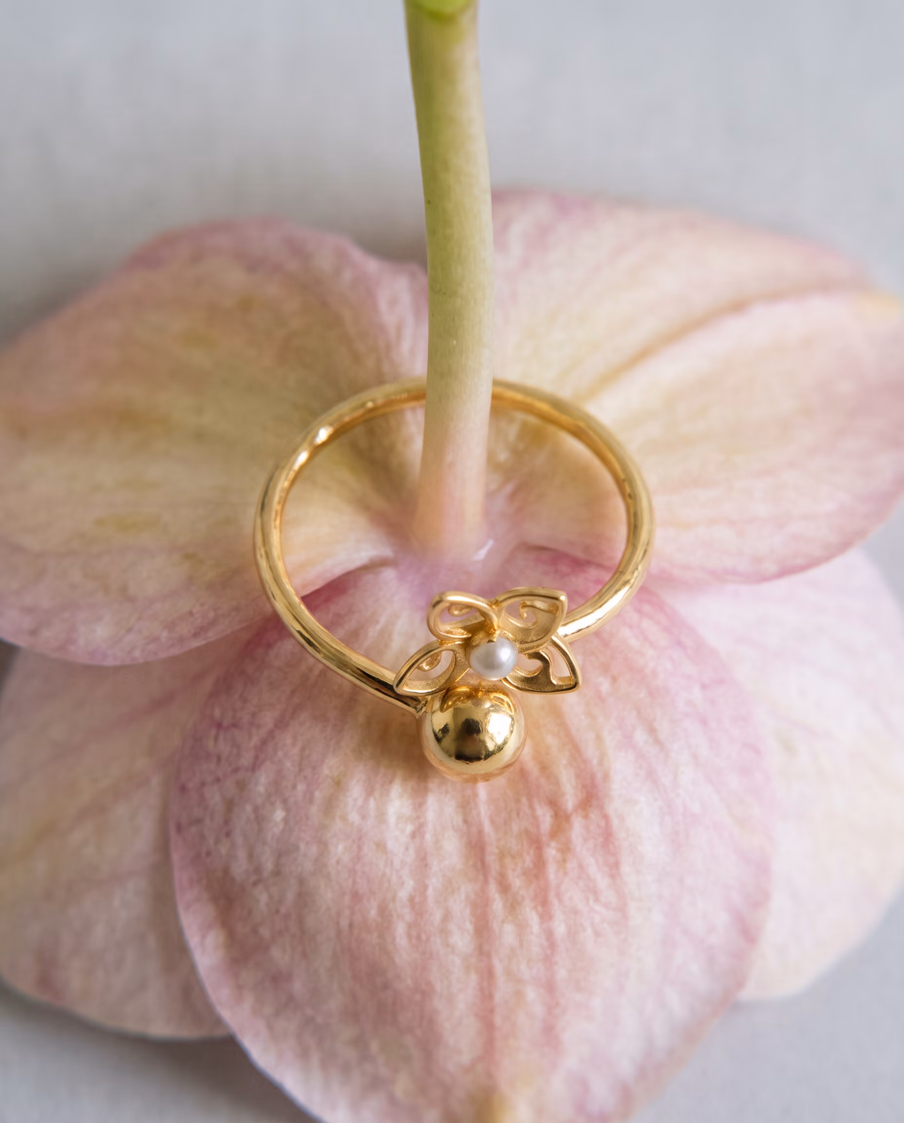 Gold ring with decorative flower and small pearl resting on a pale pink flower petal.
