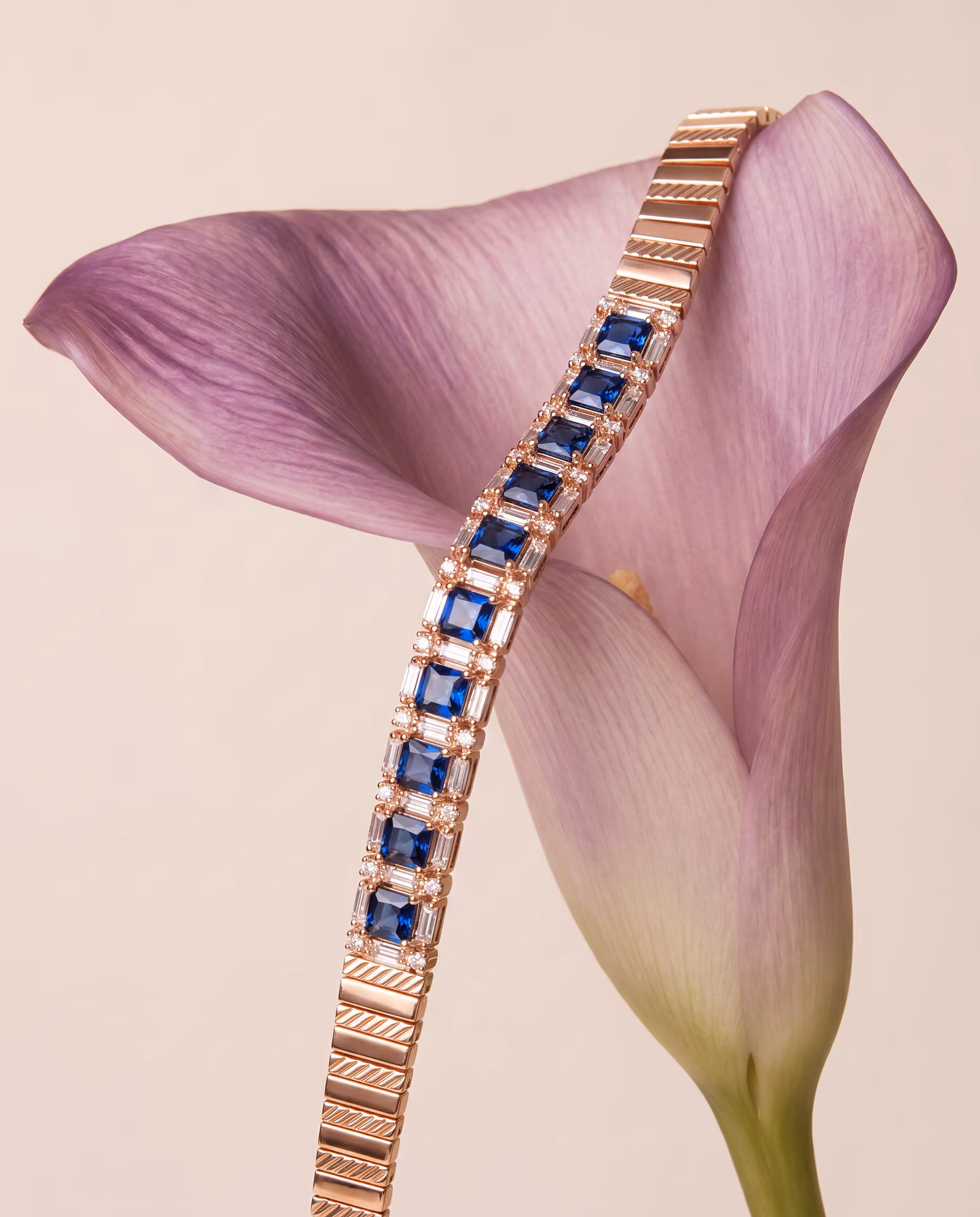 Gold bracelet with blue square gemstones and clear accents draped over light purple calla lily flower.