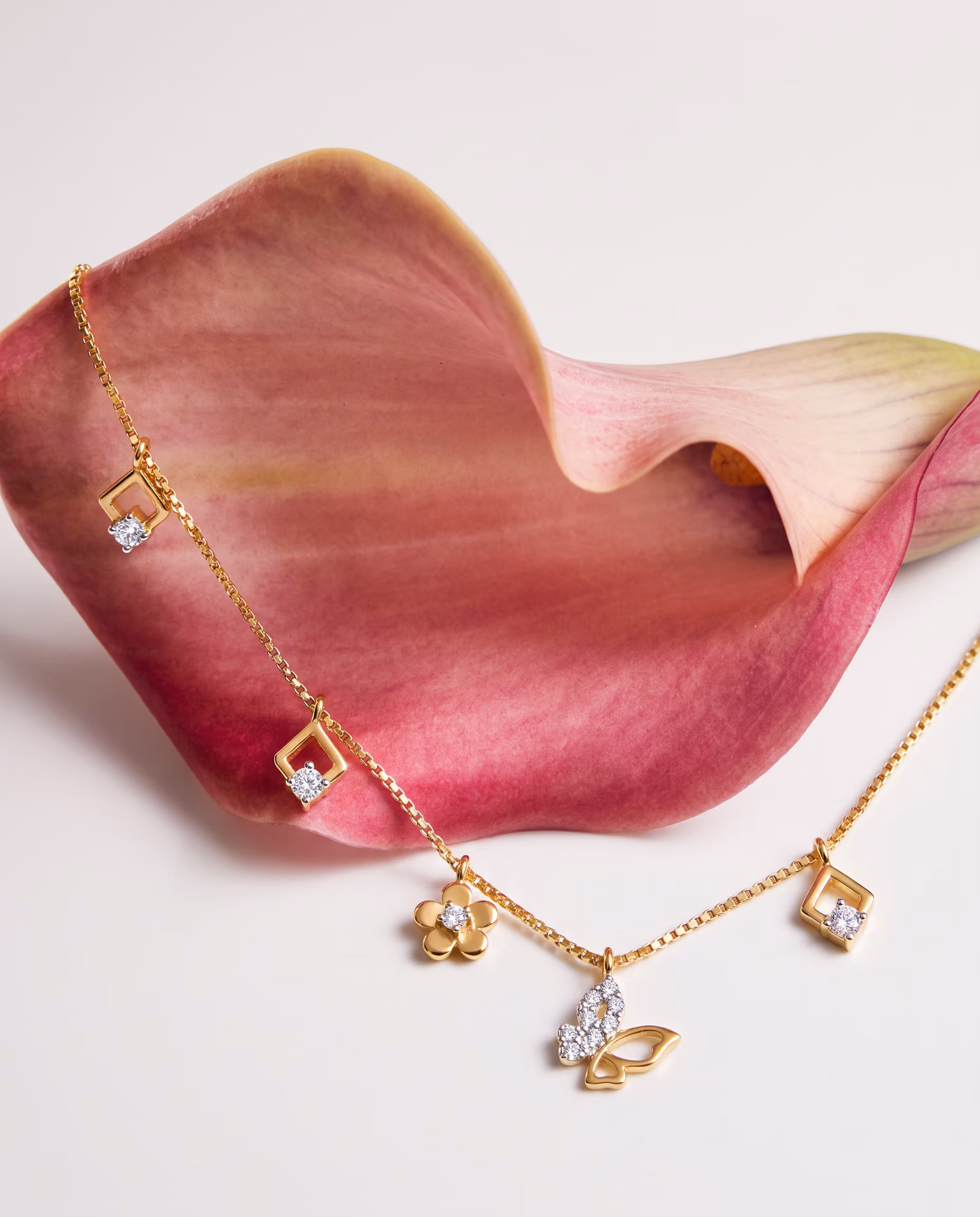 Gold charm bracelet with diamond-like accents on a pink calla lily flower background.