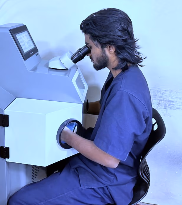 Man in blue scrubs using a microscope with gloved hands inside a laboratory machine.