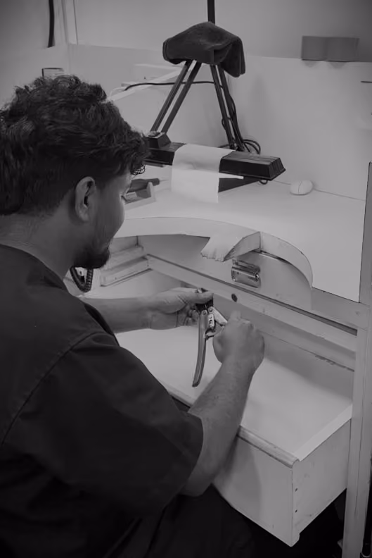 A man working with a hand tool at a white workbench under a desk lamp.