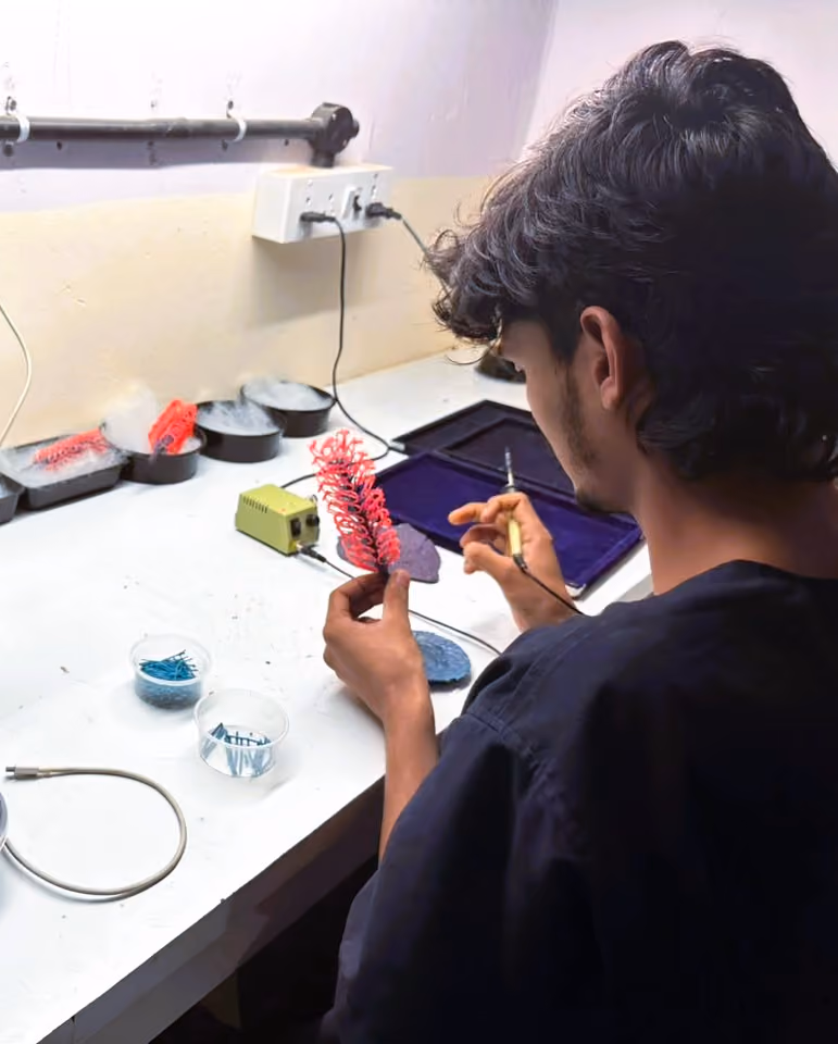 Person shaping a red plastic spiral piece using a heated tool at a white workbench.