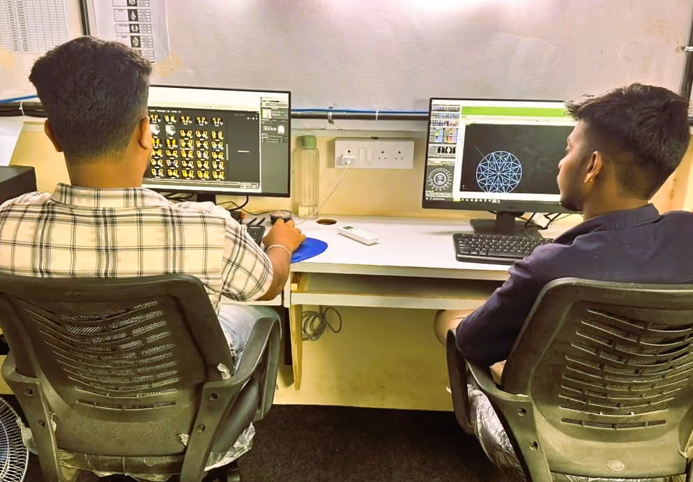 Two men sitting at desks working on desktop computers with graphic designs on screens.