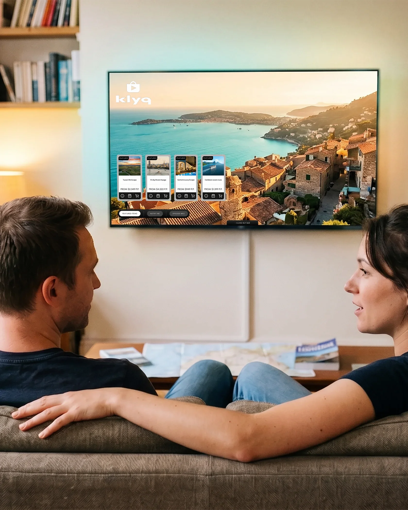 Couple sitting on a couch browsing travel deals on a TV showing the Klyq buy bar.