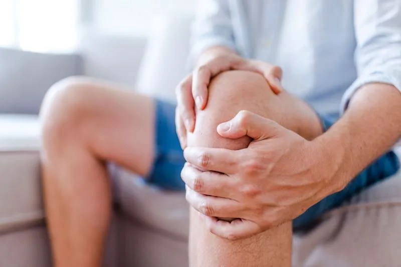 A man holding his knee while sitting on a couch.