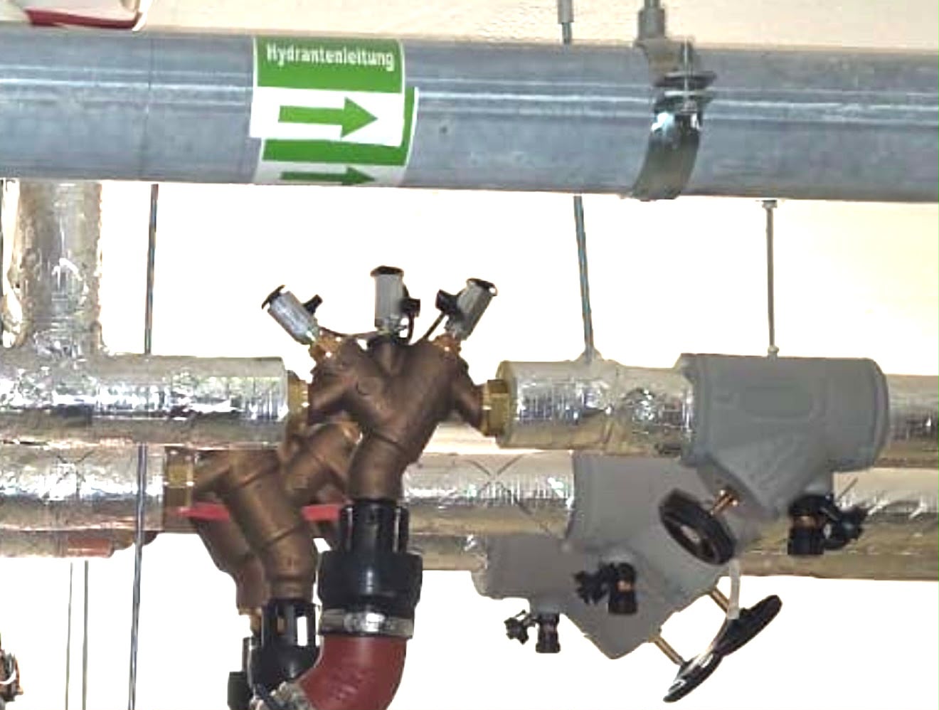 Hydrantenleitung-Pfeilschild an Metallrohren und Ventilen in einem Gebäudetechnikraum.
