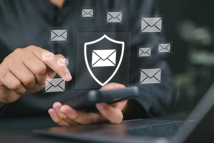 Person uses a smartphone with digital email icons and a shield symbol, highlighting security. Background is dark, emphasizing focus.