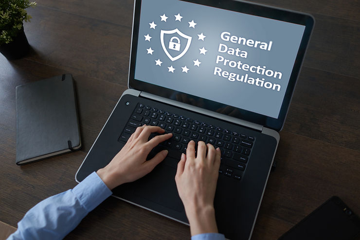 Hands typing on a laptop displaying General Data Protection Regulation with a shield icon, on a desk with notebook and phone.