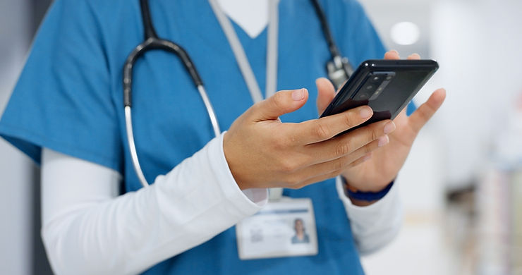 A person in blue scrubs with a stethoscope uses a smartphone in a hospital setting. An ID badge is visible. The scene is professional and focused.