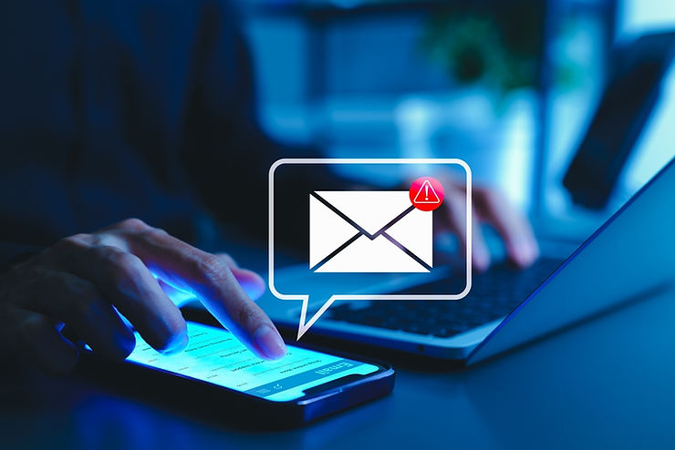 Hands using a smartphone and laptop under blue light. Email alert icon with red exclamation point overlaid, suggesting urgency or warning.