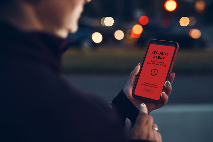 Person holding a phone with a red screen displaying a "Security Alert" message. Showing a compliance risk