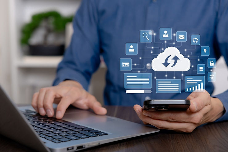 Person uses a laptop and smartphone, with cloud computing icons floating above, suggesting digital connectivity. Background is blurred.