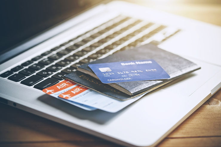 Credit card, passport, and boarding passes on a laptop keyboard. Bright lighting suggests travel planning. Blue card reads "Bank Name."