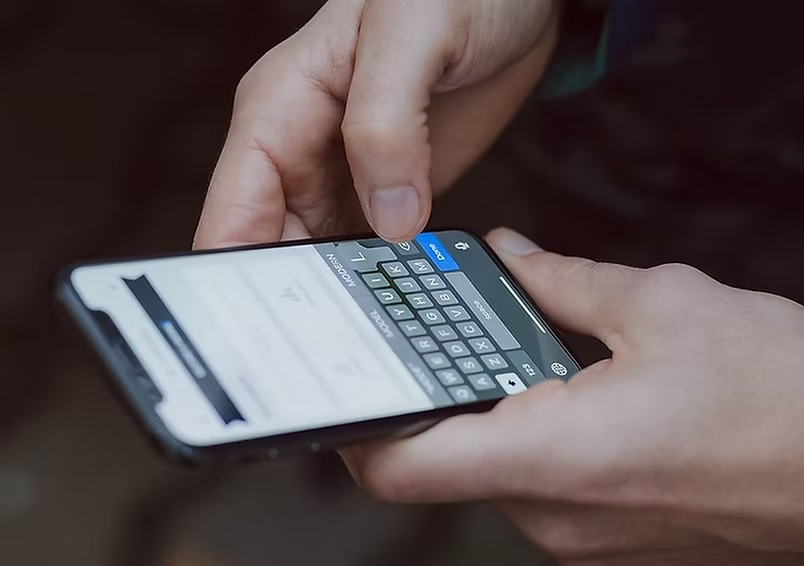 Hands typing on a smartphone screen showing a text input interface. The background is blurred, focusing on the fingers and device.