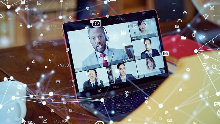 Laptop screen showing a video conference with six people in a digital network overlay. Background has a wooden table and papers.