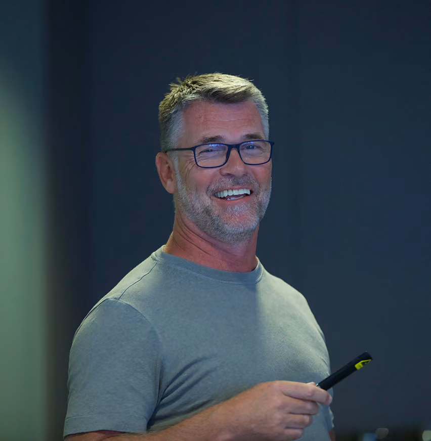 Smiling middle-aged man with glasses holding a black marker against a dark background.