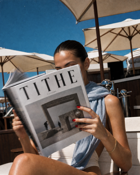 A woman reading a TITHE magazine poolside.