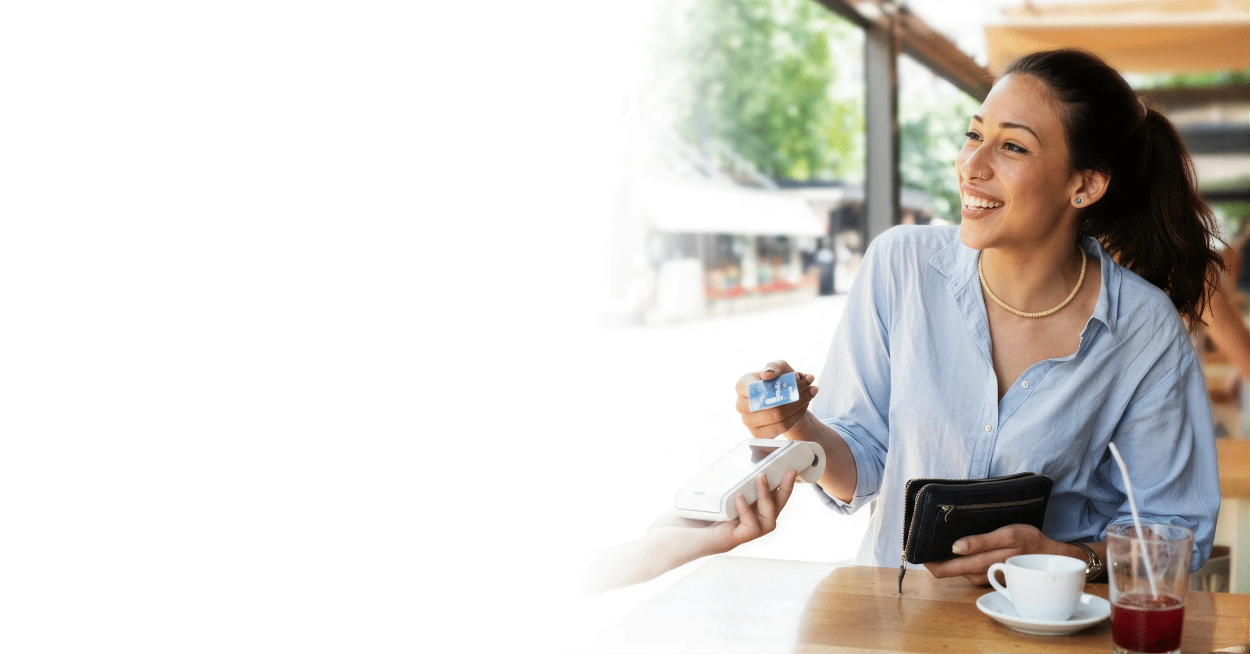 Smiling woman holding credit card paying with a card reader at an outdoor cafe table.
