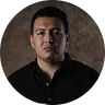 Portrait of a man with short dark hair wearing a black shirt against a gray textured background.