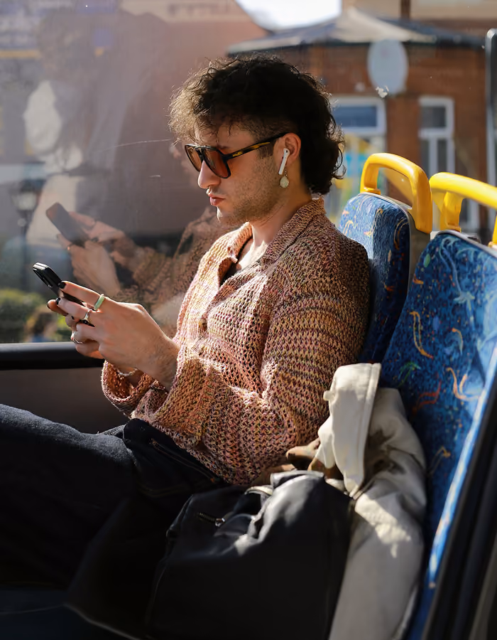 Young person in purple sweater lying on rust-colored couch using a laptop with headphones around neck.