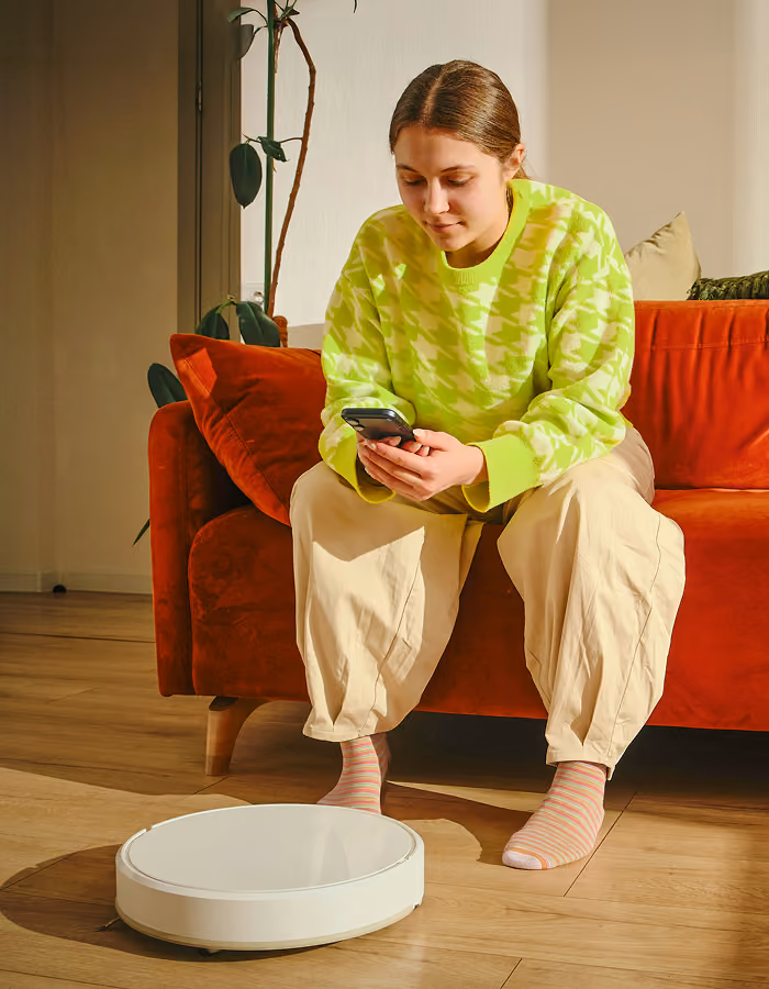 Young person in purple sweater lying on rust-colored couch using a laptop with headphones around neck.