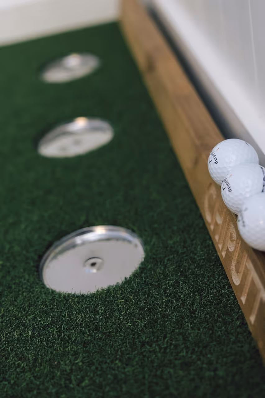 Indoor putting green with three golf holes and golf balls on wooden edge labeled cold brewing.