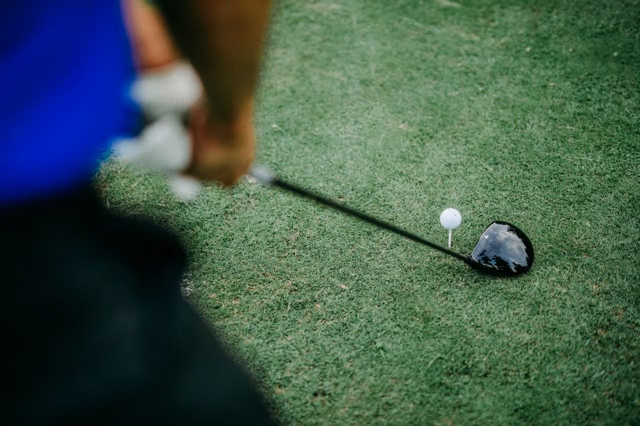 Close-up of a golfer holding a club ready to hit a golf ball on a grassy course.