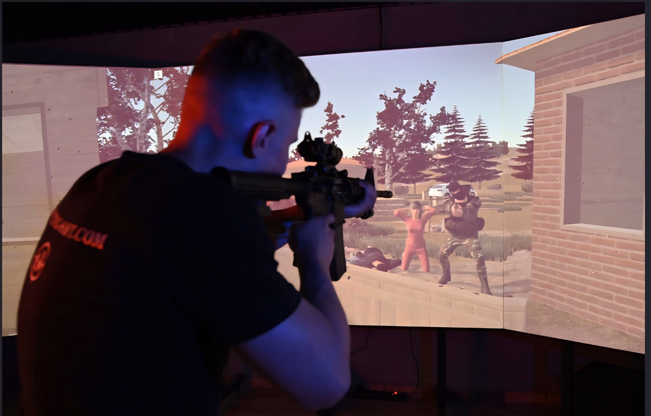 Person aiming a rifle at a screen showing a tactical simulation with armed and unarmed virtual characters.