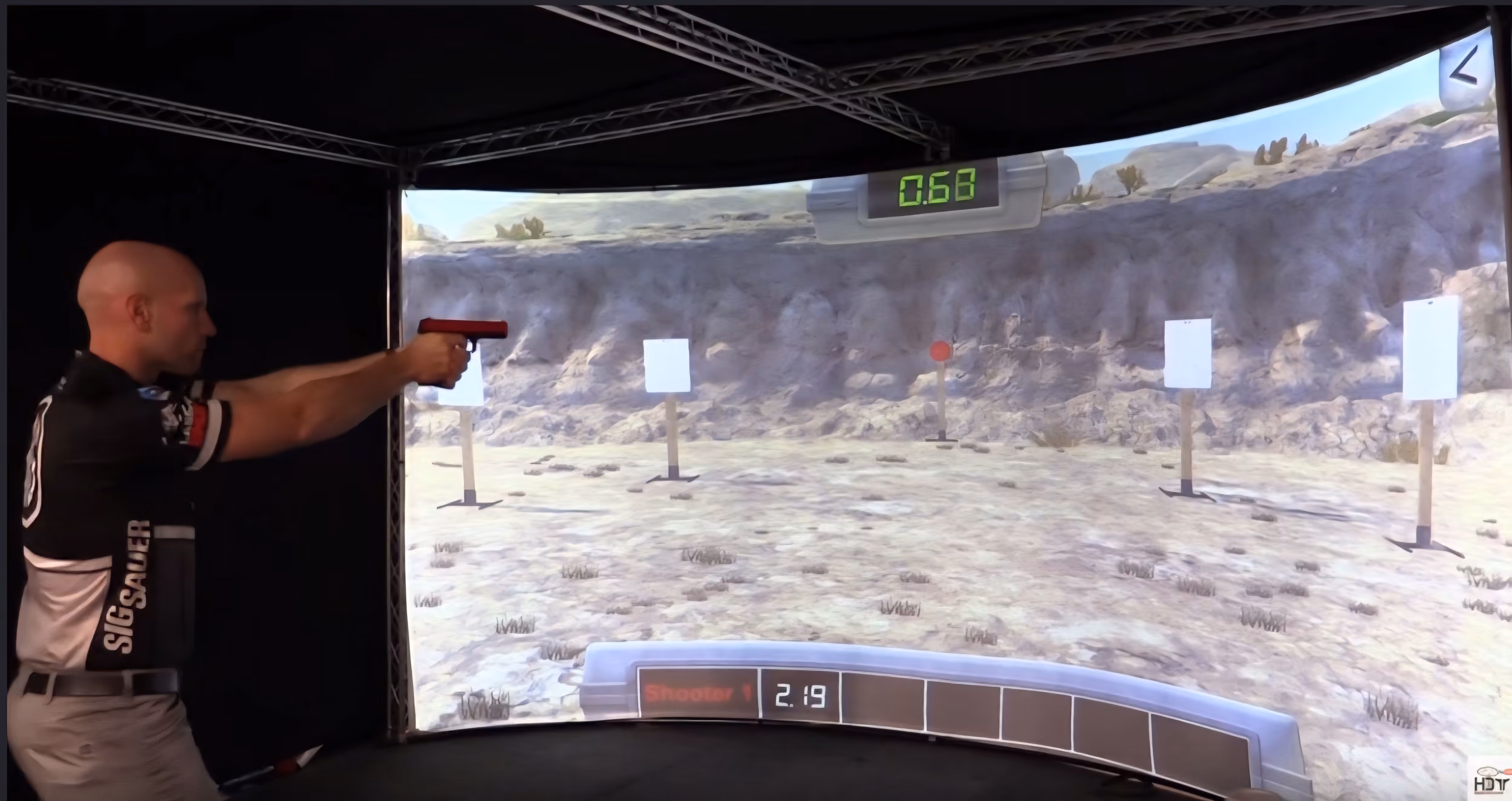 Man aiming a pistol at virtual shooting range targets projected on a curved screen.