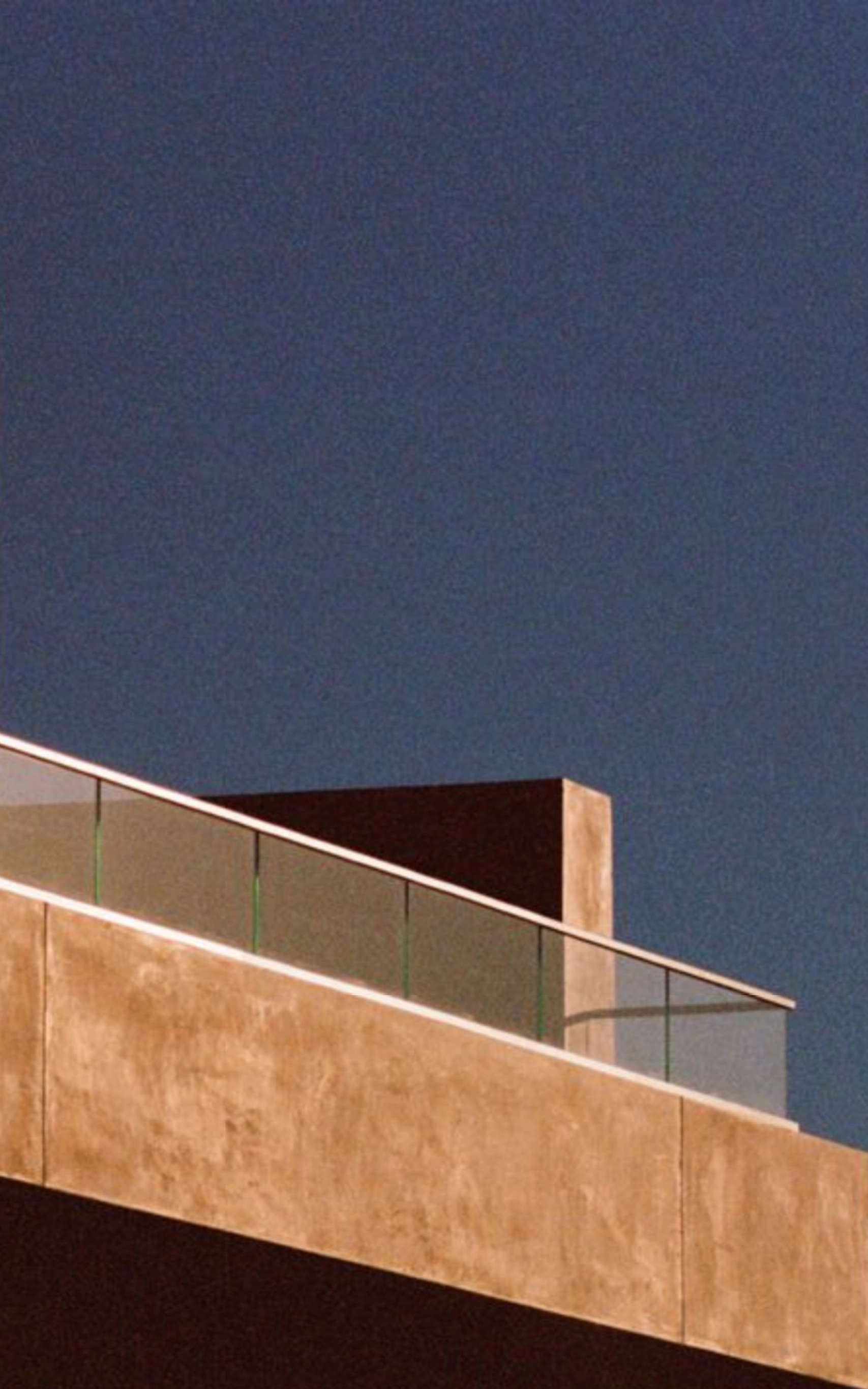 Modern building rooftop with beige concrete railing and clear glass panels under a clear blue sky.