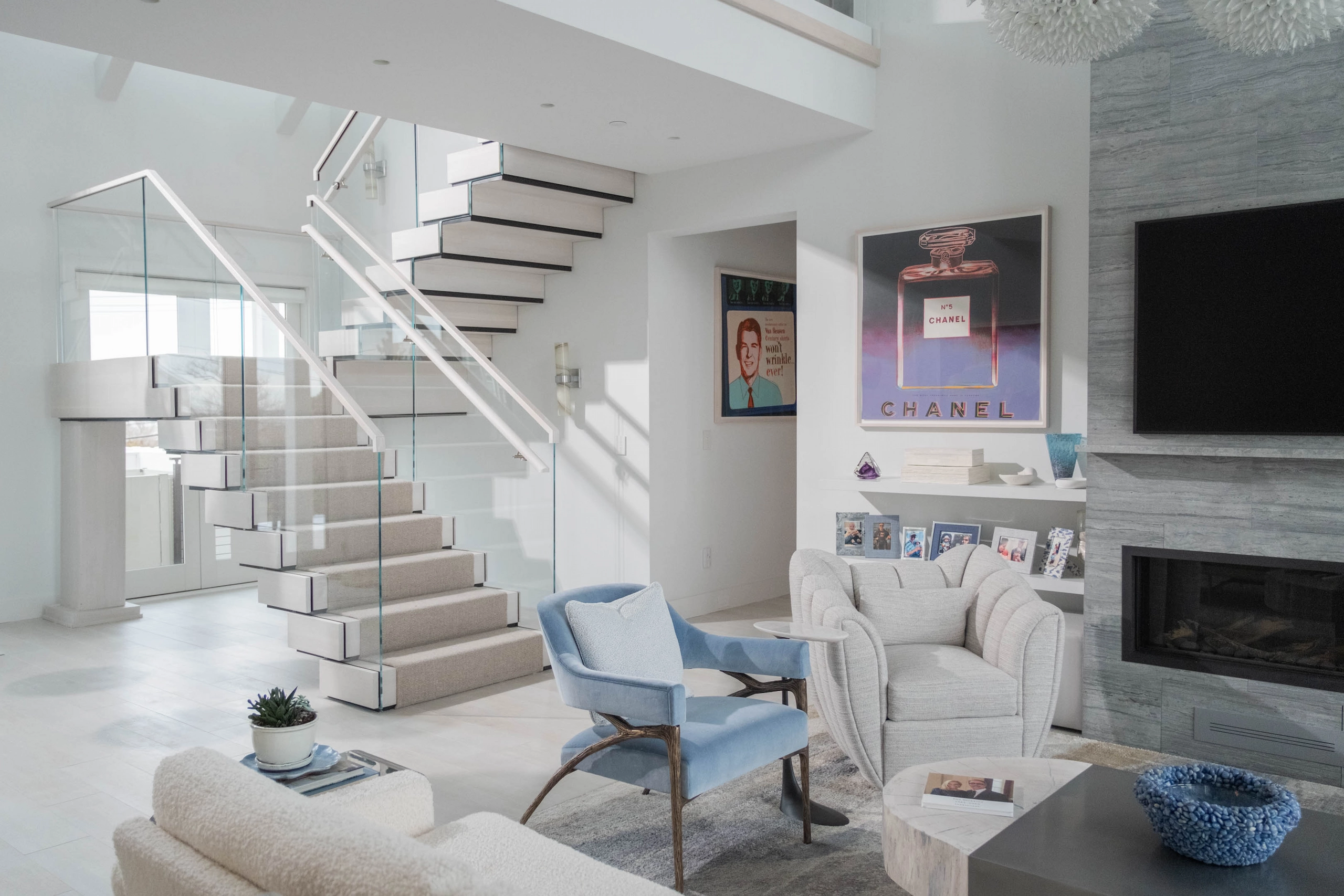Modern living room with FLIGHT Stack staircase, light blue armchair, beige chairs, and fireplace under TV.