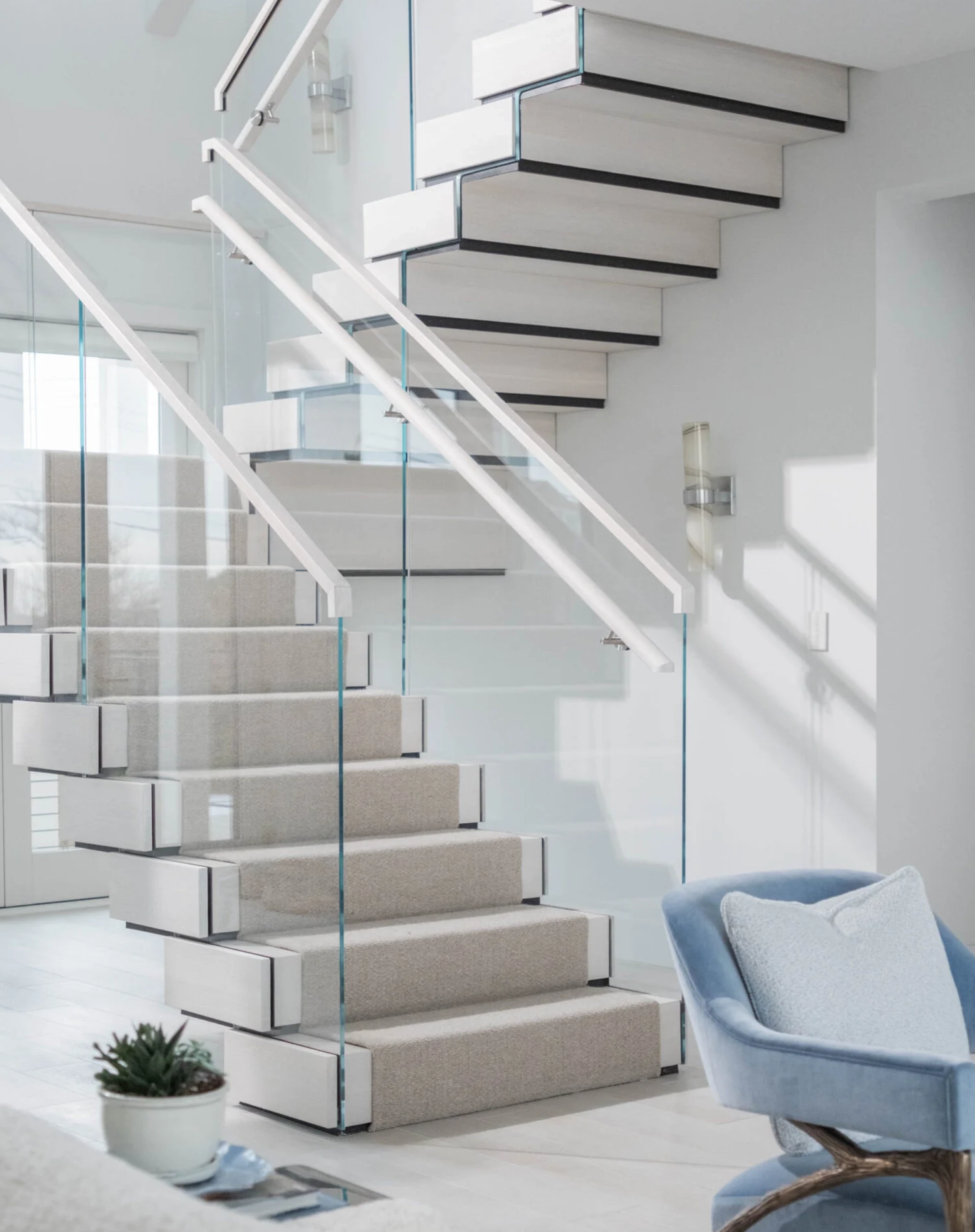 Modern floating staircase with glass railings and beige carpet in a bright room.