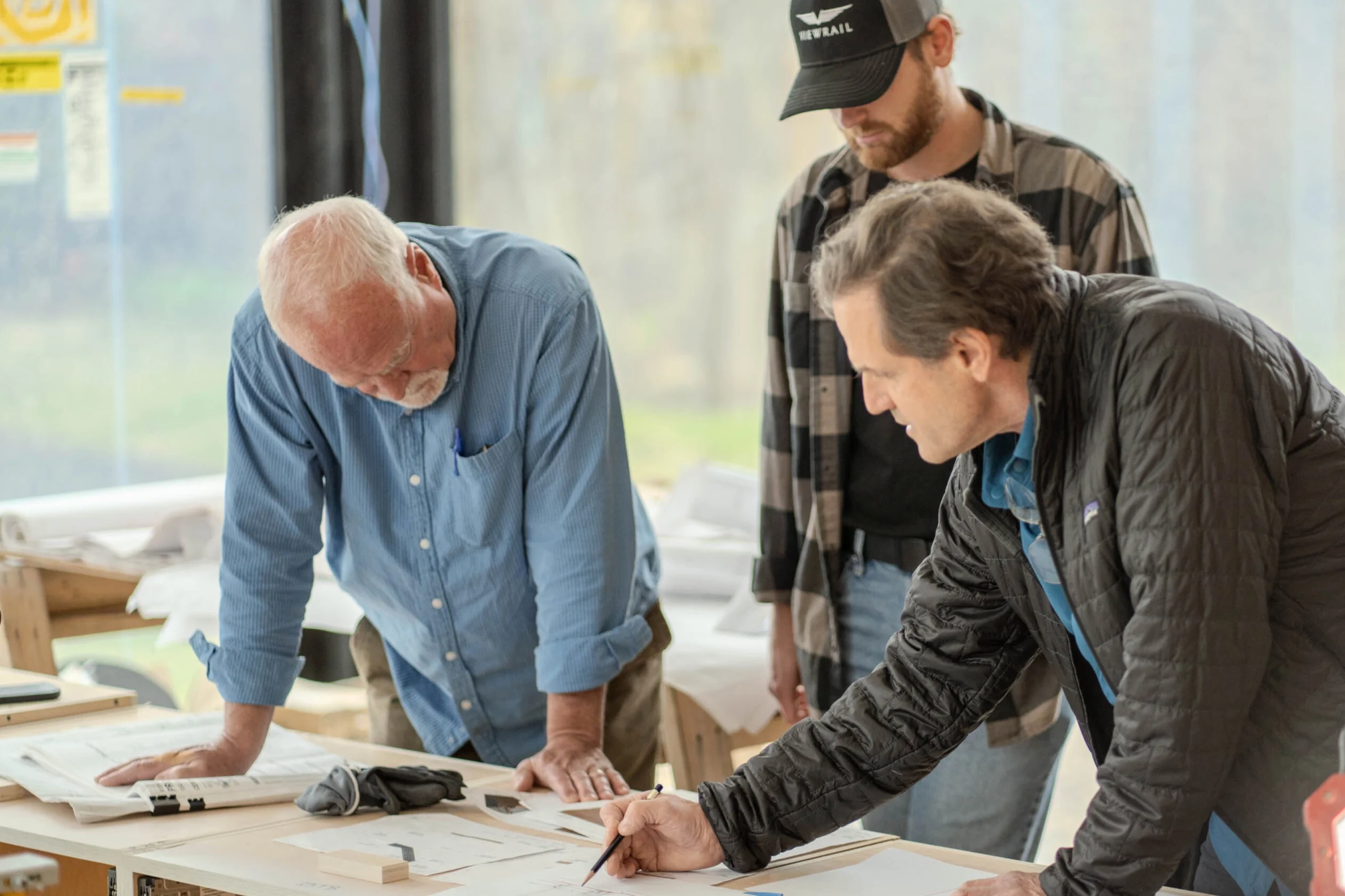 Three men reviewing architectural plans on a table in a bright workspace.