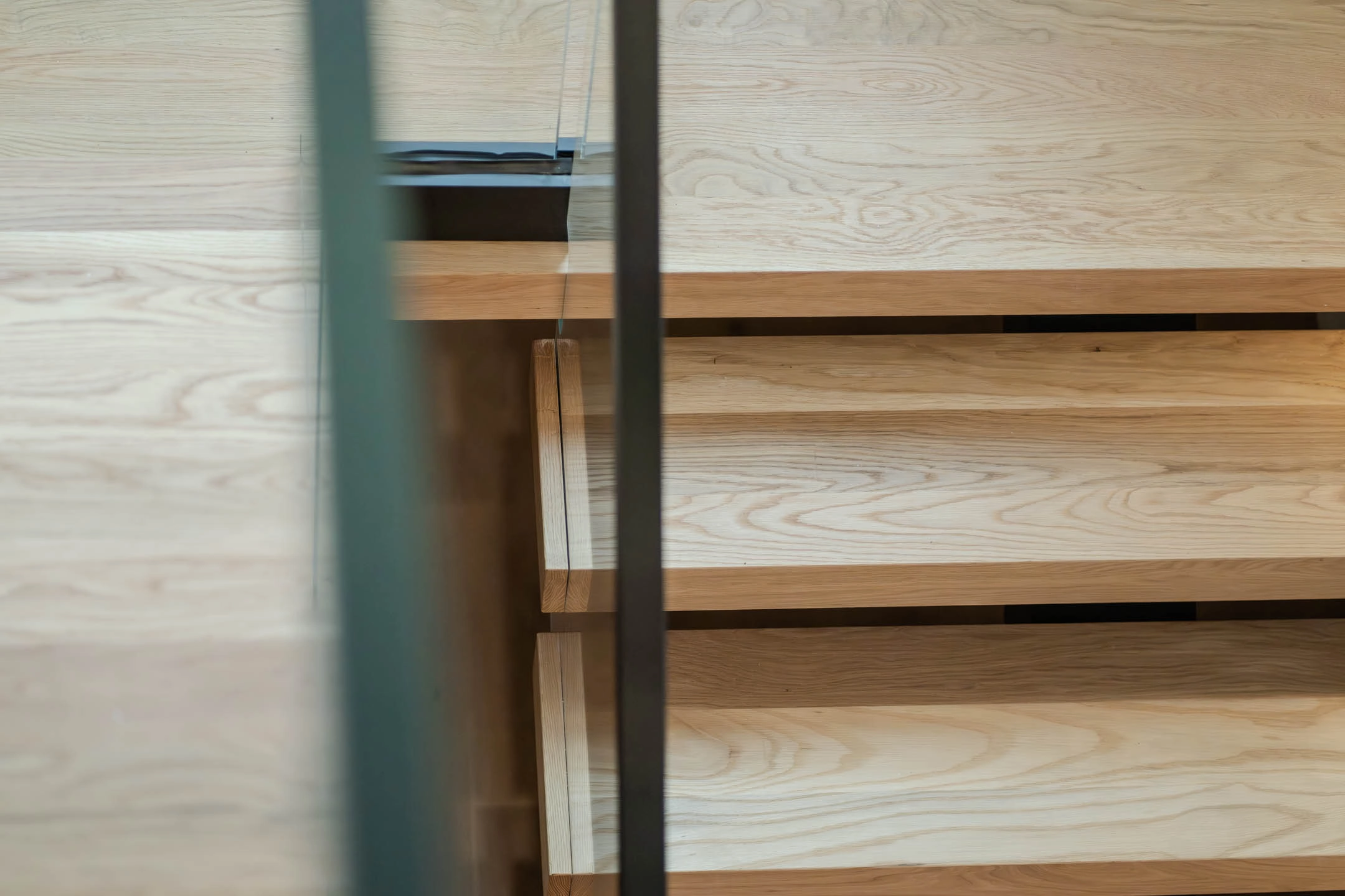 Close-up of wooden stairs viewed from above through a glass railing panel.