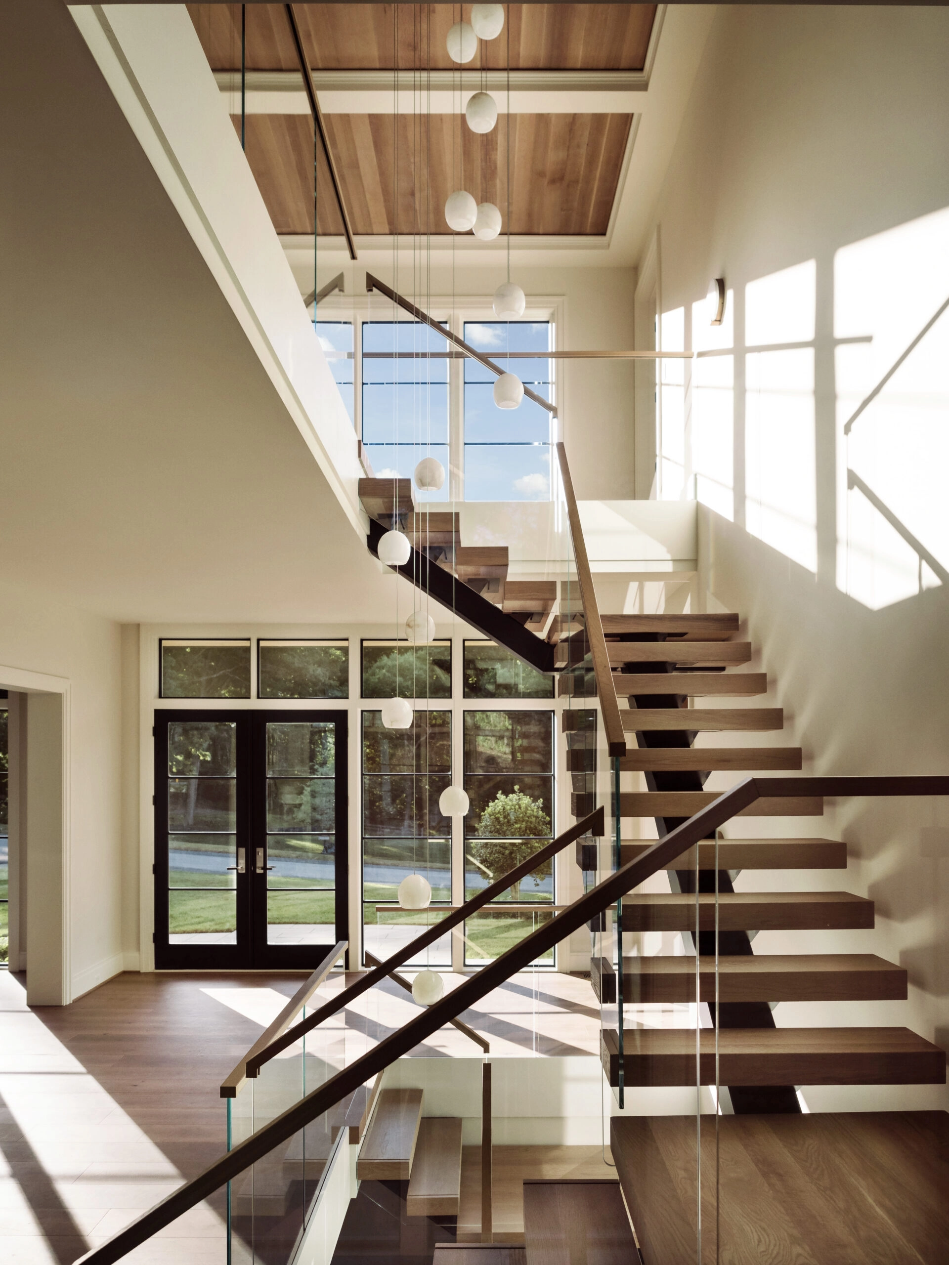 A FLIGHT Mono stair rises through a two-story entry under a wood-panelled ceiling