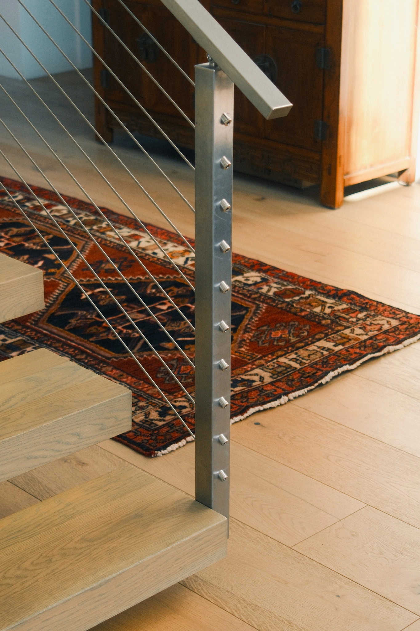 At the foot of a stair, a stainless Signature Cable post stands over a patterned rug