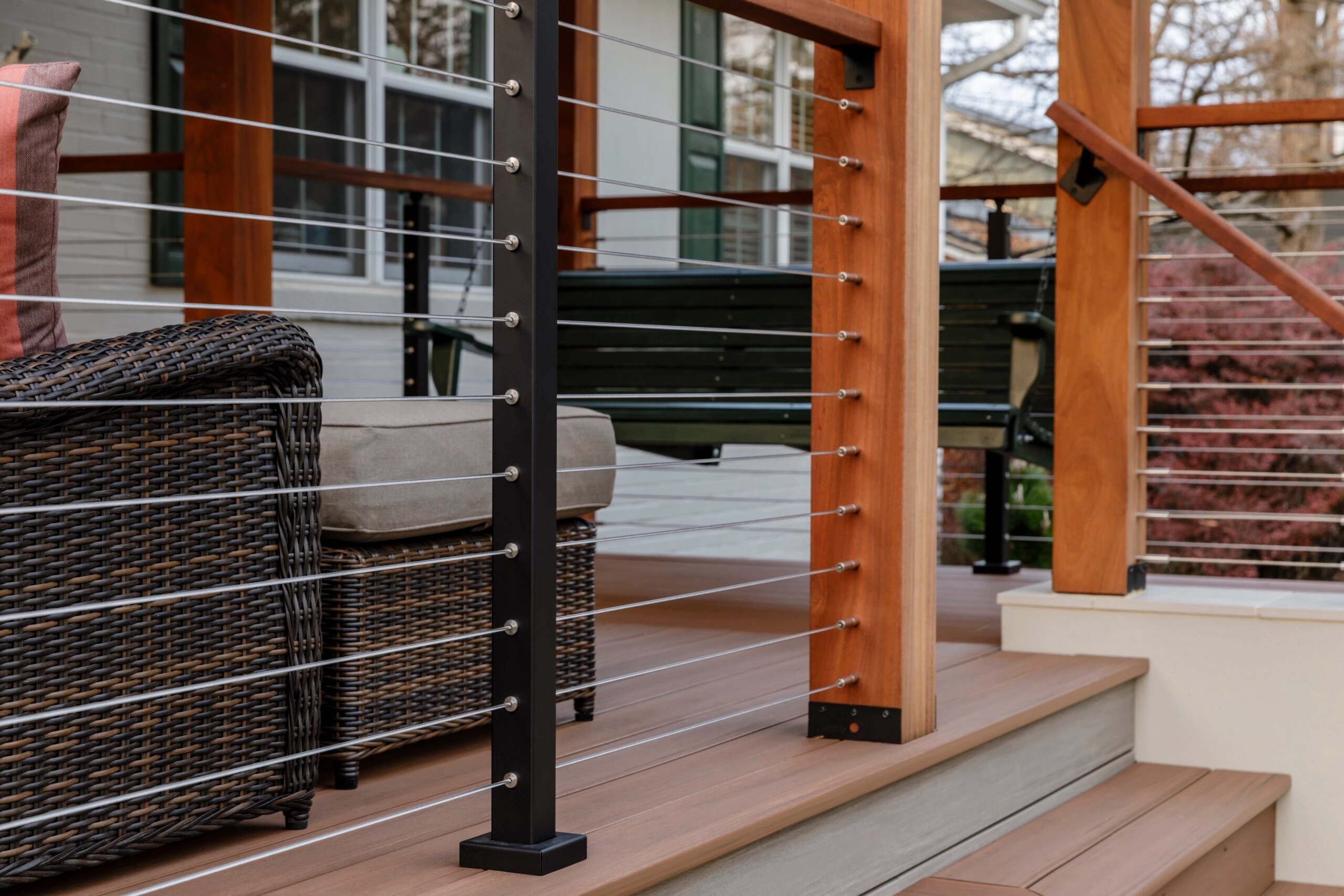 A black post and a wood post share a run of DriveTite cable beside deck steps and wicker seating