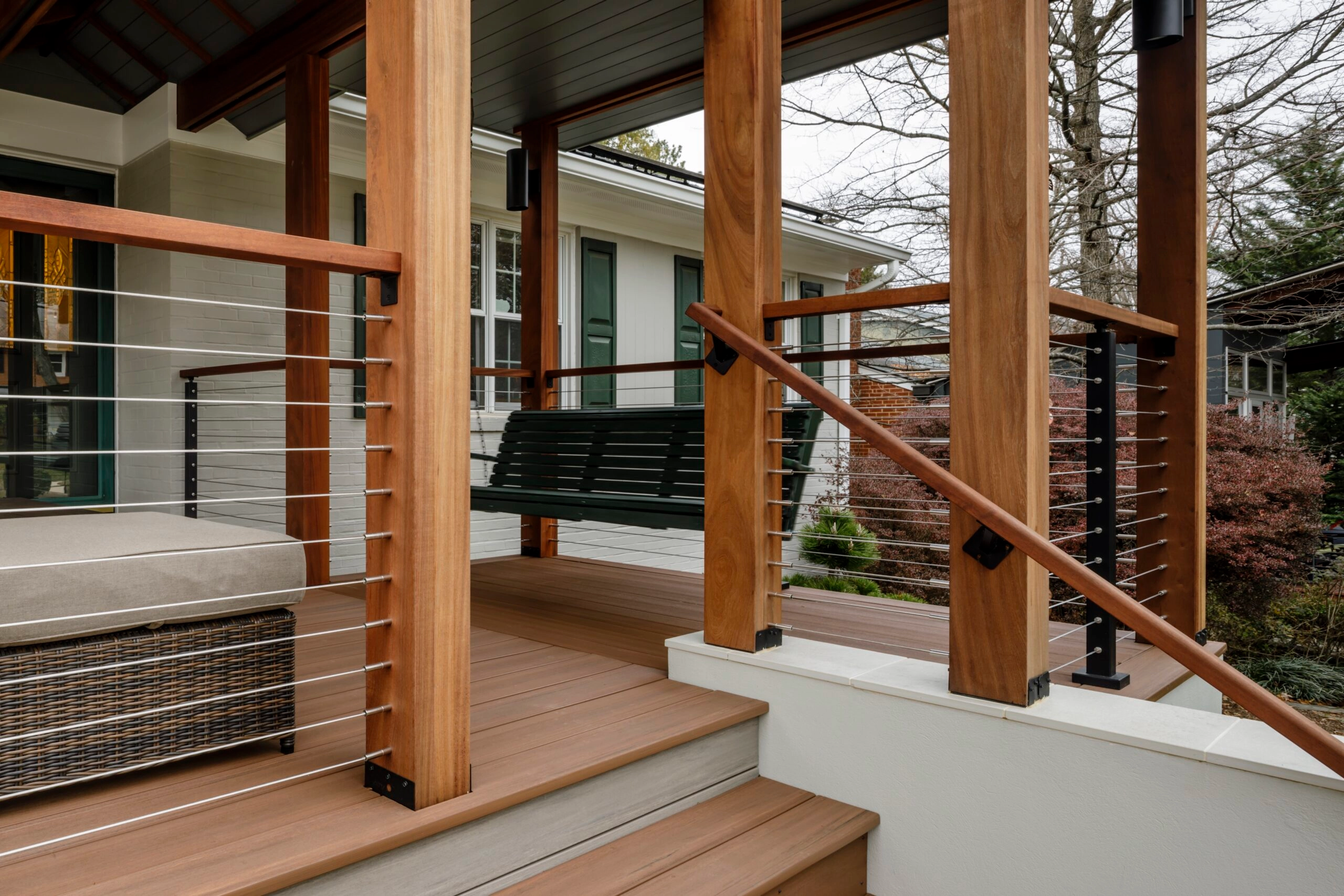 Wicker seating and a hanging swing on a porch, black DriveTite posts holding cable under wood rail