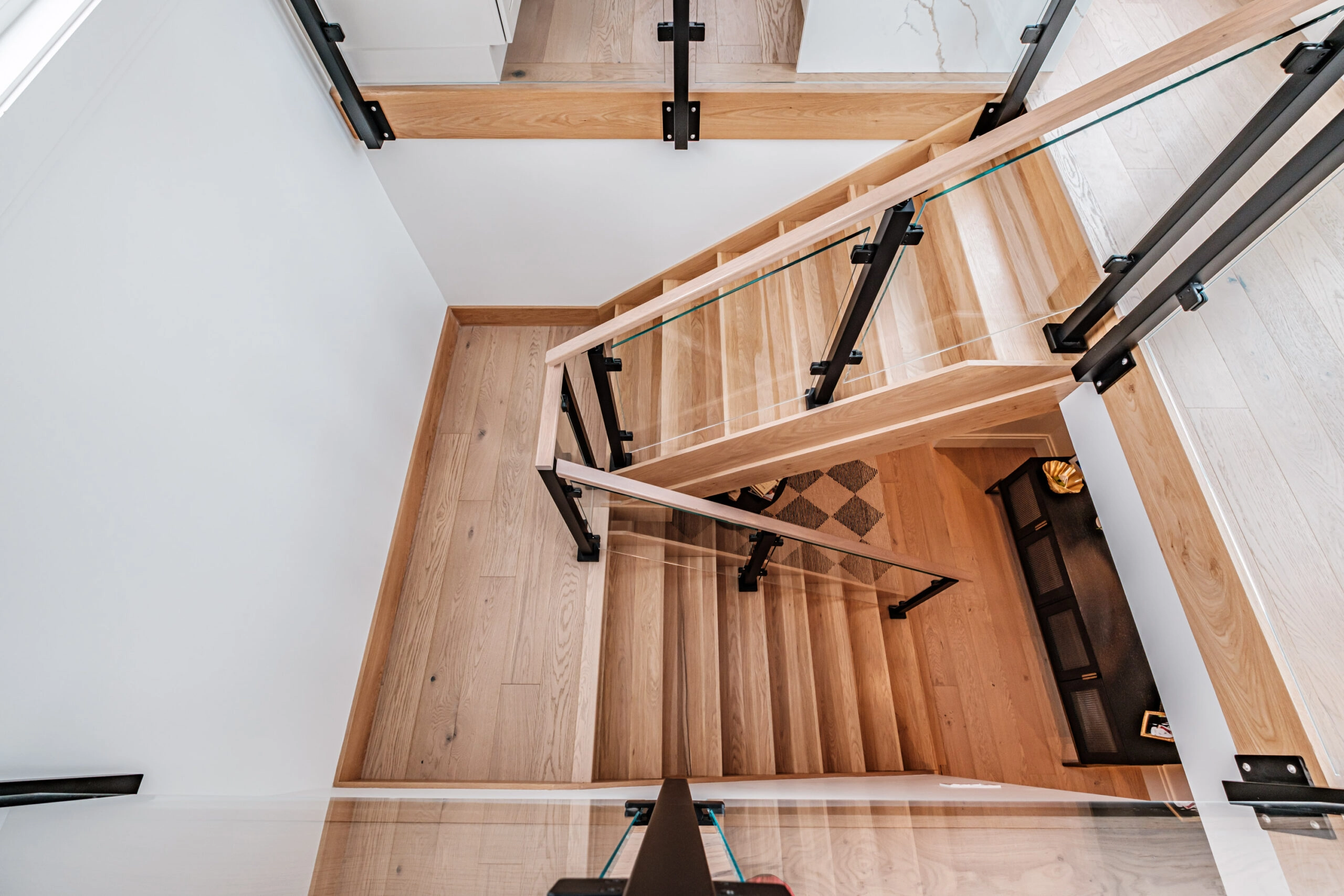 Straight down onto wood stair treads, black post plates and glass panels around the opening
