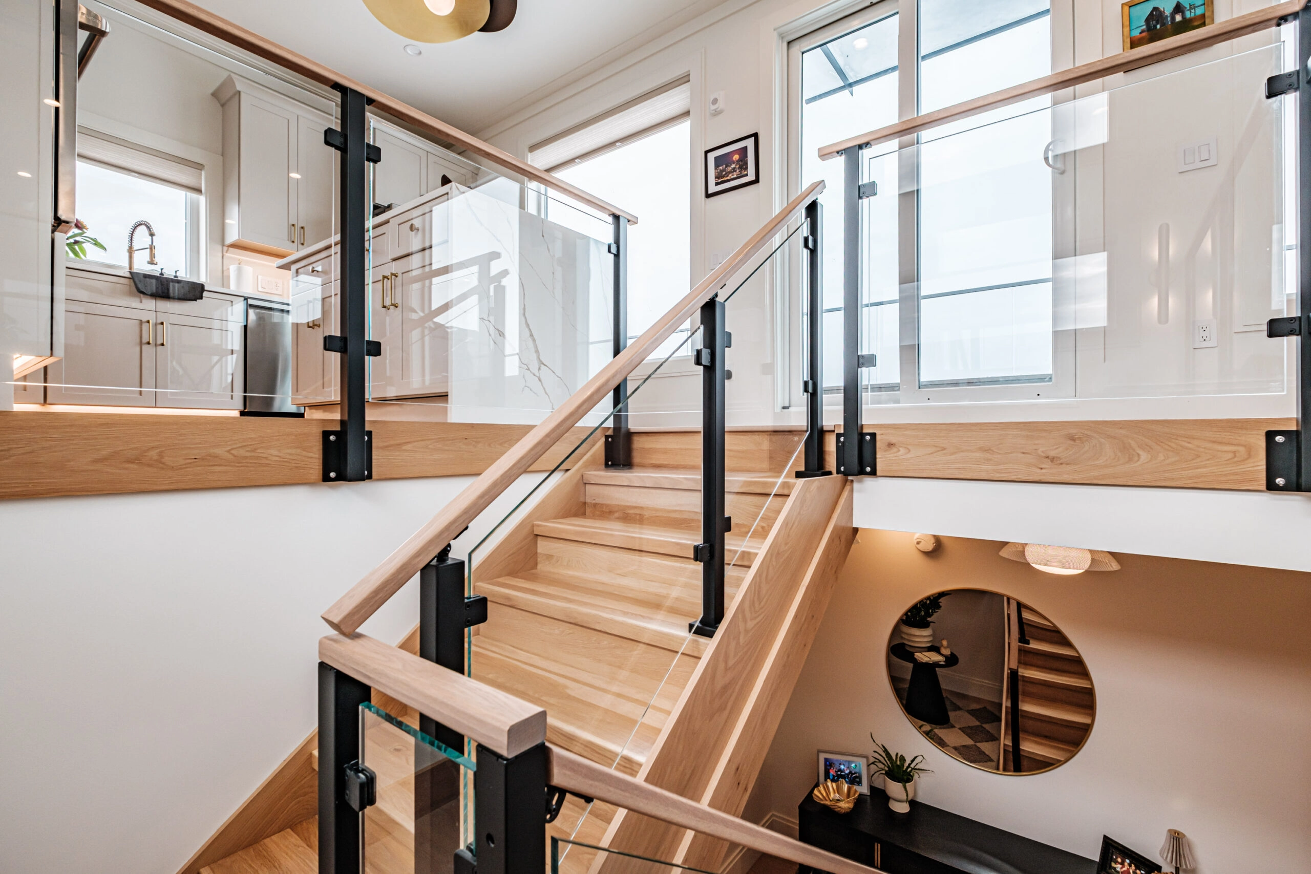 Glass panels and a wood top rail on black posts wrap a stair landing beside the kitchen