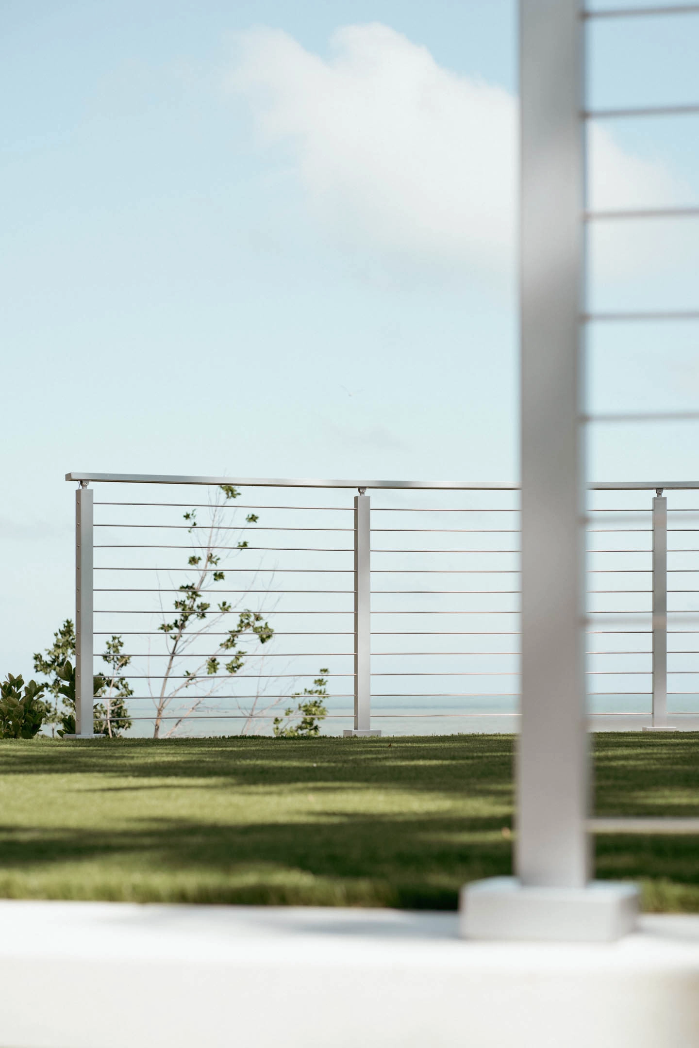 Stainless Signature Rod railing edges a lawn above the sea, one post close in frame